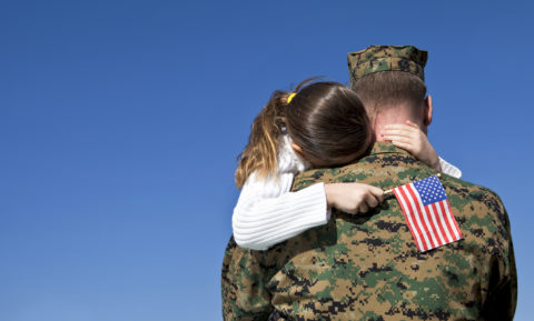 Man in uniform holding his daughter that has an american flag in her hand