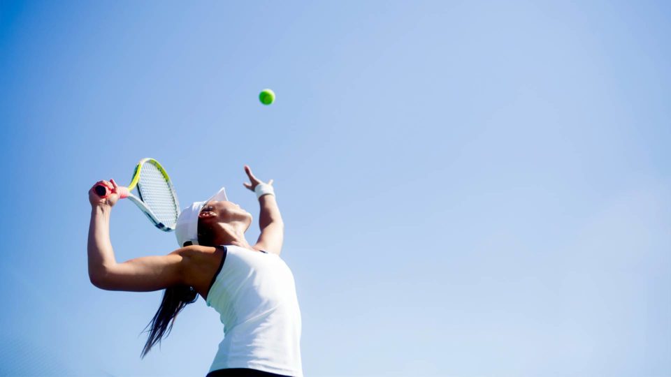 woman playing tennis outside in the sun with a blue sky in the background