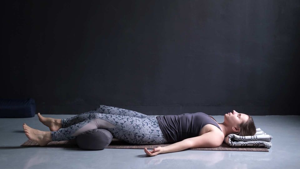woman laying down in a dark room with yoga props in savasana practicing yoga nidra